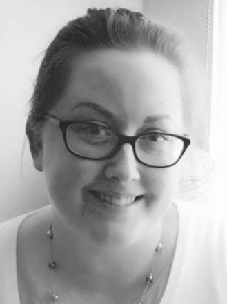 Smiling woman with glasses and a necklace, captured in a black and white portrait.