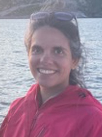 Smiling woman wearing a red jacket with water in the background.